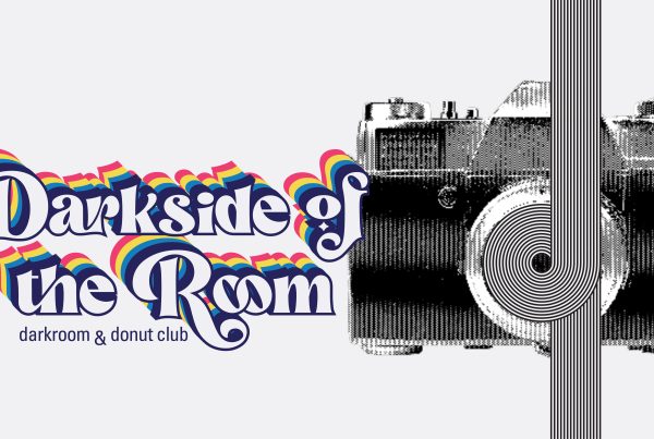 A 70s-inspired font with rainbow shadows reads “Darkside of the Room: darkroom and donut club”. To the right, a halftone image of a SLR camera with black and white geometric lines curving around lens.